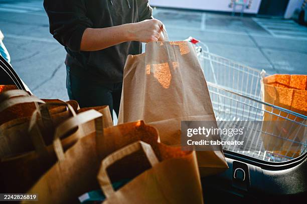 person loading paper grocery bags into car trunk - overloaded shopping cart stock pictures, royalty-free photos & images