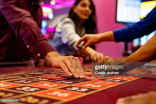 spieler, die ihre wetten machen, während sie roulette in einem casino spielen - roulettetisch stock-fotos und bilder