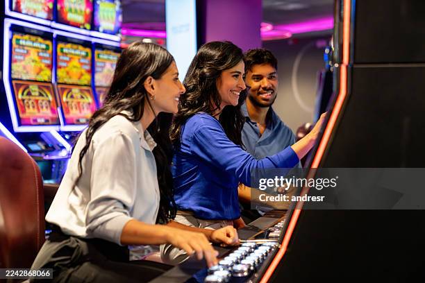 feliz grupo de amigos en un casino jugando en las máquinas tragamonedas - casino interior fotografías e imágenes de stock
