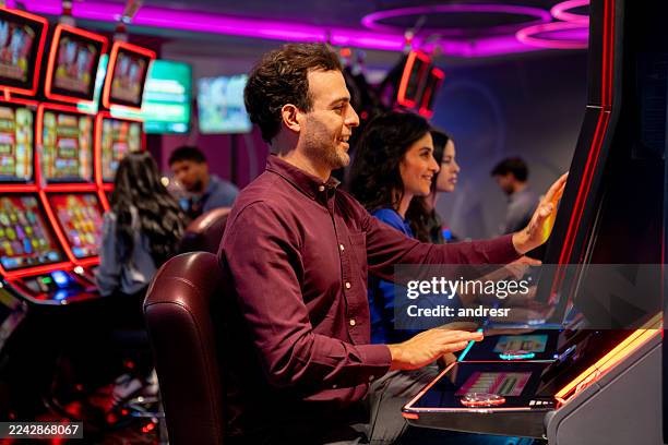 groupe de personnes heureuses jouant sur les machines à sous d’un casino - casino interior photos et images de collection