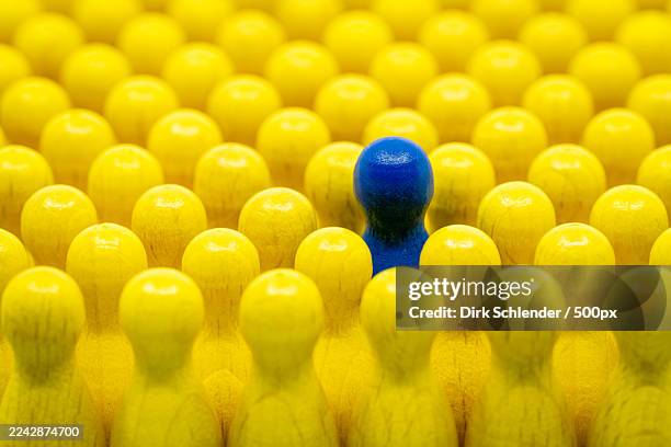 a single blue wooden peg stands out among a large group of yellow wooden pegs, symbolizing individuality and distinction - gegensatz stock-fotos und bilder