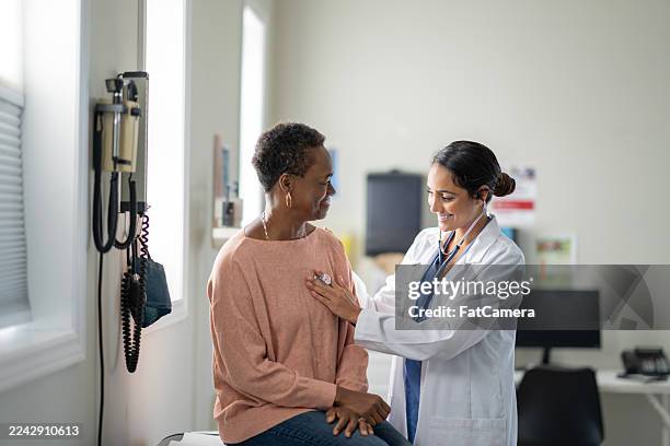 caring hispanic female doctor examines african american senior woman during clinic visit - primary care stock pictures, royalty-free photos & images