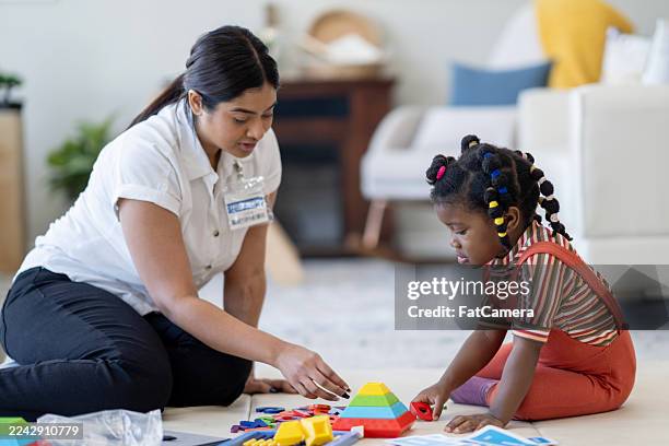 diverse female caregiver and young girl playing with colorful building blocks at home together happily - child care worker stock pictures, royalty-free photos & images