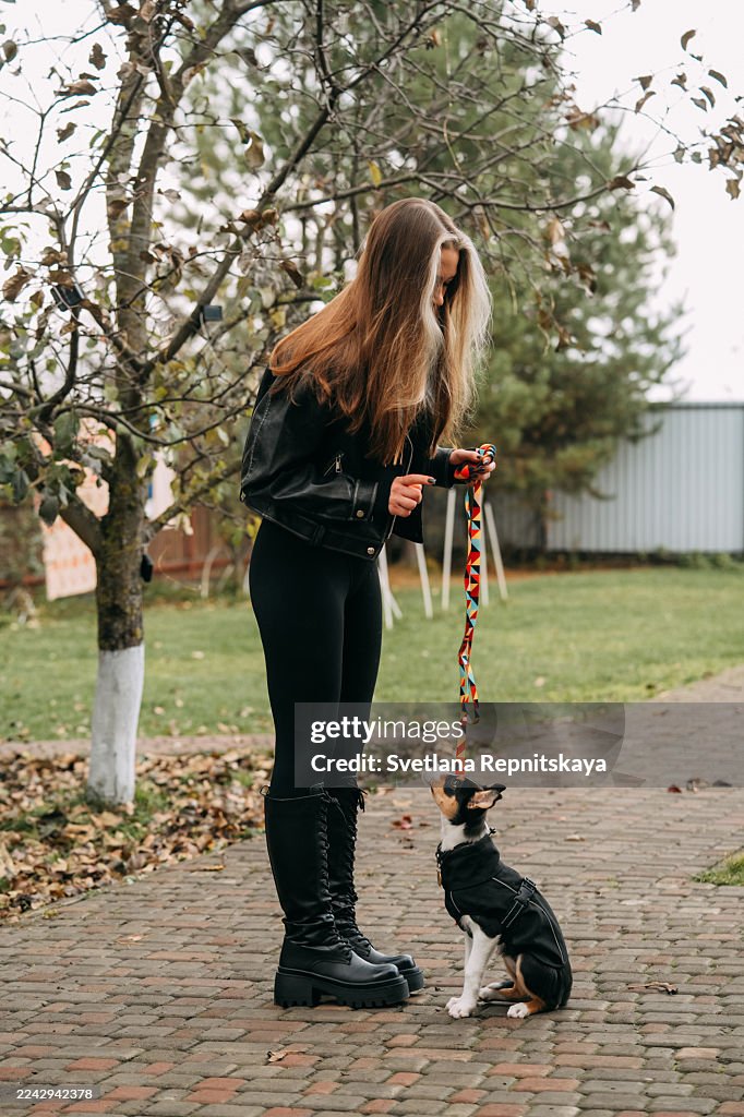 Woman training puppy on leash outdoors in autumn