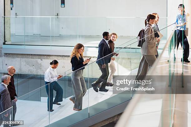 diverse professionals ascend a modern glass staircase in a bright corporate office lobby - balustrade stock pictures, royalty-free photos & images