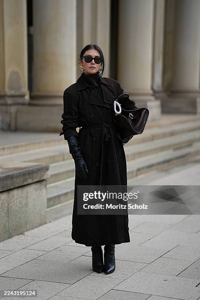 Milena Karl is seen wearing a long belted trench coat in dark brown with collar and lapel details by Ducie London; covering a dark brown knit turtle...