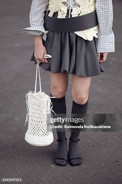 Mari Airapetyan wears a grey pleated mini skirt paired with a checked shirt layered under a yellow crochet vest, wide grey leather belt, styled with...