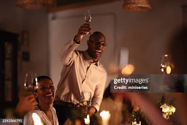 friends celebrate dinner with raised wine glasses in warm evening lighting and laughter - gala stock pictures, royalty-free photos & images
