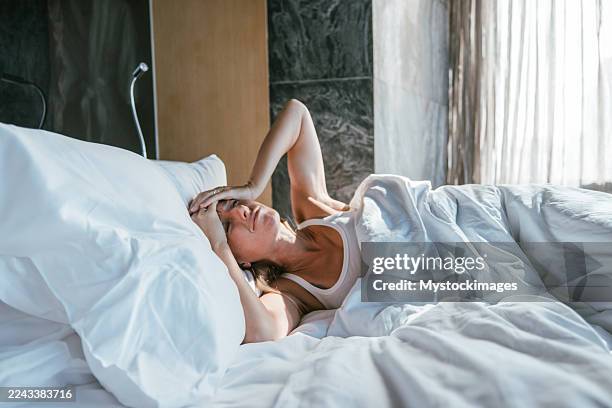 woman lying in bed with headache - slapeloosheid stockfoto's en -beelden