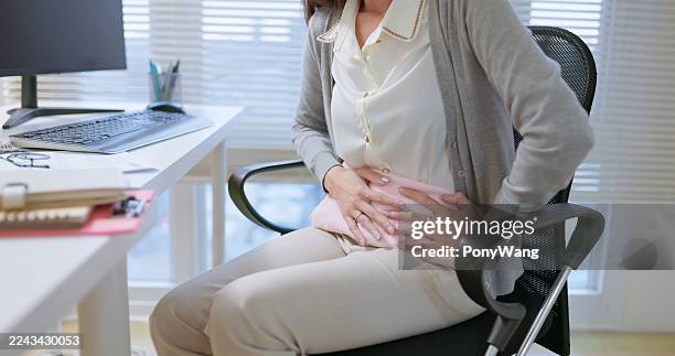 asiatische geschäftsfrau verwenden bauchheizkissen büro - wärmflasche stock-fotos und bilder