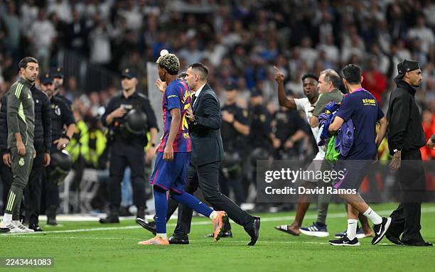 Lamine Yamal of FC Barcelona is escorted off the pitch as Vinicius Junior of Real Madrid reacts as he gestures towards him as they leave the pitch...