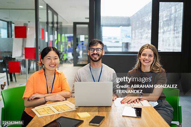 equipo empresarial diverso sonriendo a la cámara, sentado en una mesa de reuniones en una oficina moderna trabajando en colaboración - el trabajo en equipo hace que el sueño funcione fotografías e imágenes de stock