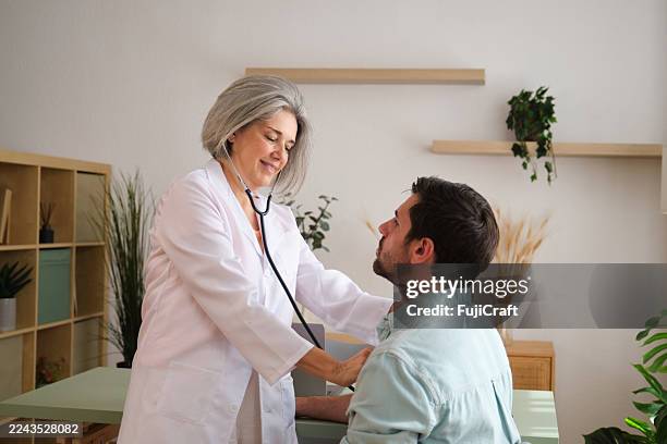 female doctor examining patient with stethoscope in medical office - cuidados de saúde primários imagens e fotografias de stock