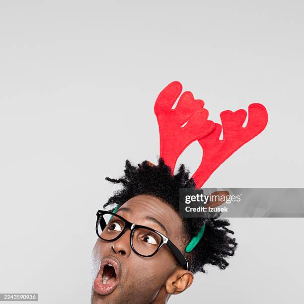 christmas portrait of surprised nerdy man wearing reindeer headband hores - antler stock pictures, royalty-free photos & images