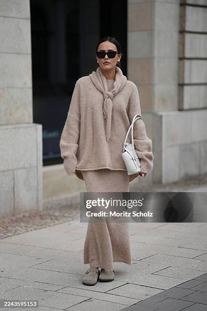 Laura Noltemeyer is seen wearing an oversized beige alpaca wool sweater with tie-back detailing by Aylin König; a long alpaca wool knit skirt in a...