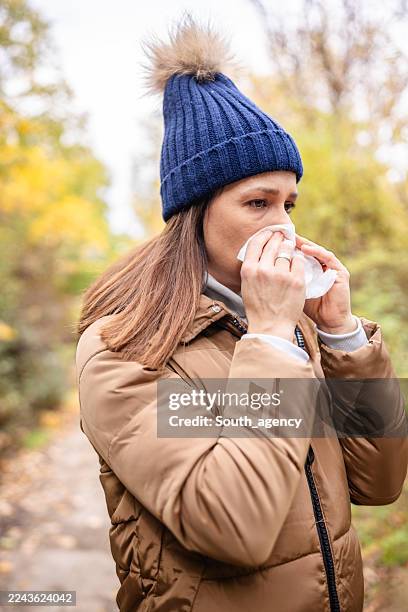 woman outdoors dealing with cold symptoms while taking a walk in a park during autumn season - immune system stock pictures, royalty-free photos & images
