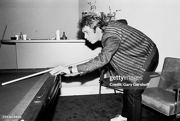 View of American Rock & Pop musician Huey Lewis as he lines up a shot with a pool cue, backstage before an interview at MTV Studios, New York, New...