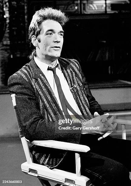View of American Rock & Pop musician Huey Lewis as he sits in a director's chair during an interview at MTV Studios, New York, New York, January 3,...