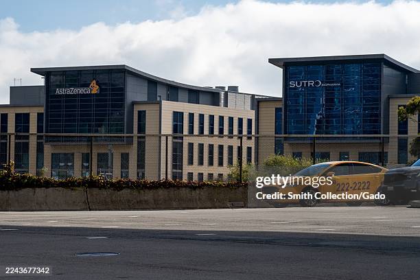 AstraZeneca and Sutro Biopharma office buildings with logos visible, viewed across street with yellow taxi in foreground, South San Francisco,...