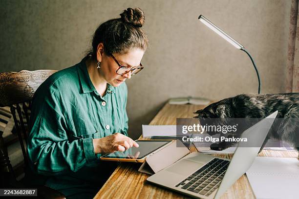 woman working from home with laptop and digital tablet with pet cat on desk - emerald green office stock pictures, royalty-free photos & images