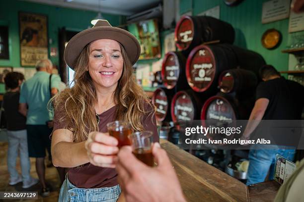 frau hält zwei shots hoch und stößt an der bar auf sherry an - jerez de la frontera stock-fotos und bilder