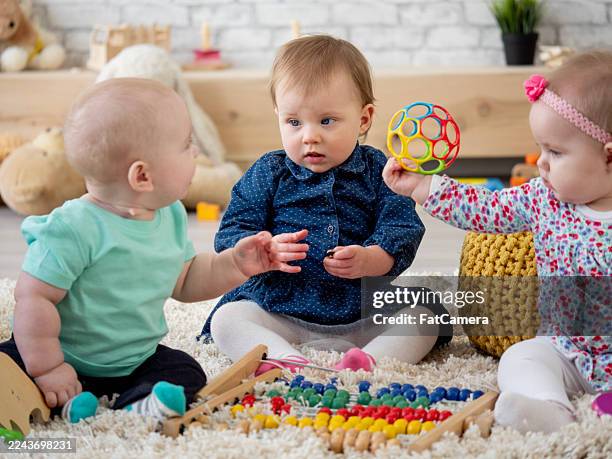 three babies playing with toys on soft rug, engaged in playful, safe home environment - gripping stock pictures, royalty-free photos & images