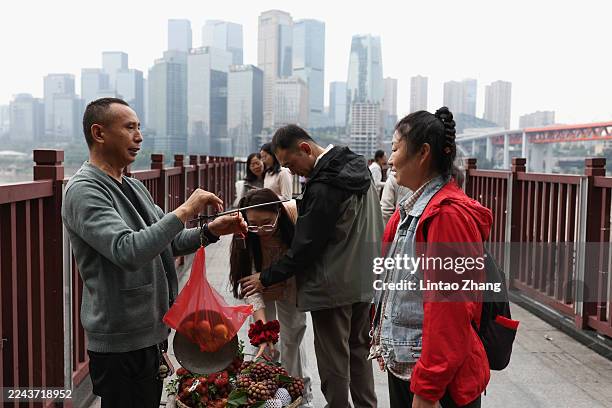 Vendor is selling fruits on a pedestrian overpass, with the city line behind them on October 28, 2025 in Chongqing, China.