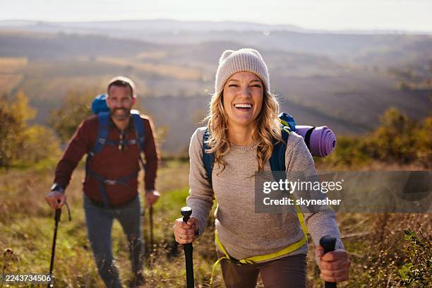 happy female hiker and her boyfriend moving up the hill in autumn day. - mid adult couple stock pictures, royalty-free photos & images