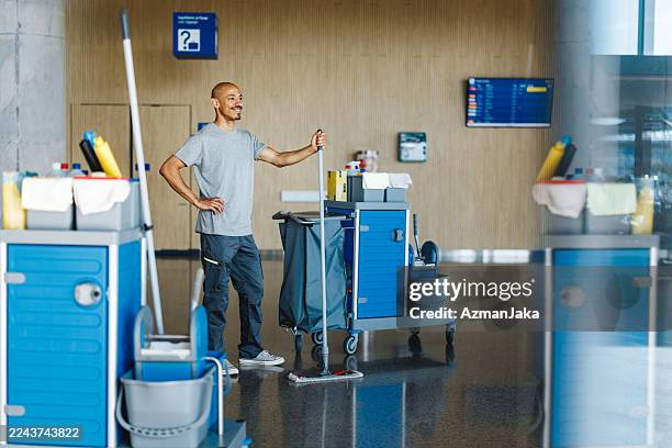 contenuto mid adulto pulitore ispanico con mocio nel luminoso terminal dell'aeroporto - impresa di pulizie foto e immagini stock
