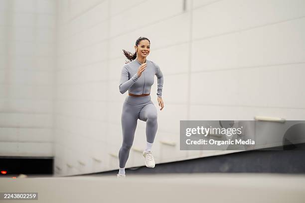 mujer corriendo cuesta arriba en ropa deportiva gris haciendo ejercicio activamente - cuesta arriba fotografías e imágenes de stock