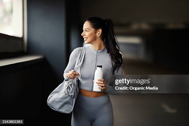 smiling young woman holding water bottle and gym bag - gym bag stock pictures, royalty-free photos & images