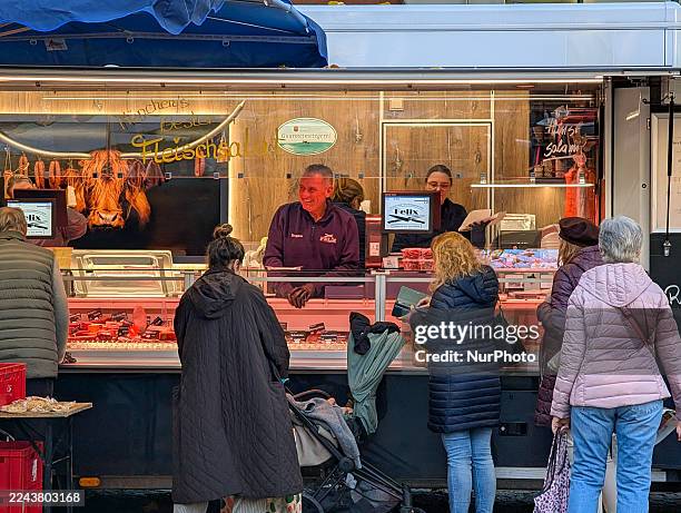 Customers queue to purchase meat and sausage products from a professional butcher stall in a market at Rotkreuzplatz in Munich, Bavaria, Germany, on...