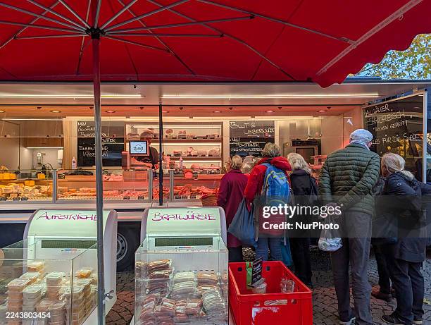 Customers queue to purchase meat and sausage products from a professional butcher stall in a market at Rotkreuzplatz in Munich, Bavaria, Germany, on...
