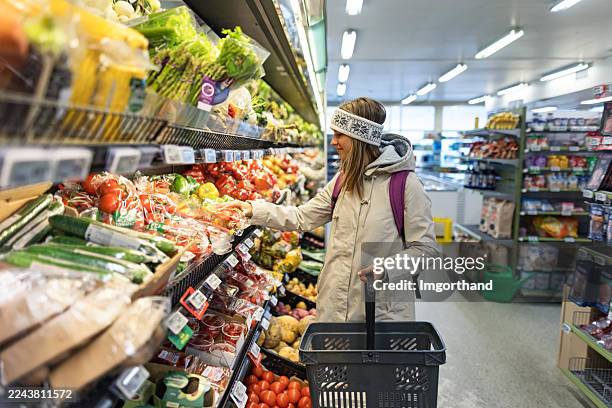 shopper in headband selects fresh produce in brightly lit grocery store aisle - stormarknad bildbanksfoton och bilder