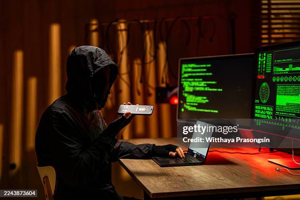hacker using phone and laptop for data breach at night - wirtschaftskriminalität stock-fotos und bilder