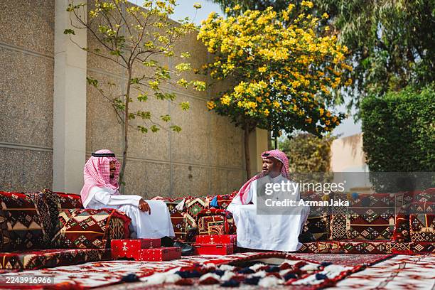 middle eastern men relaxing in traditional arabic majlis with vibrant outdoor setting - majlis stock pictures, royalty-free photos & images