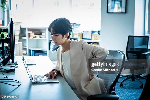 japanese businesswoman with lower back pain from long hours of desk work - lower back stock pictures, royalty-free photos & images