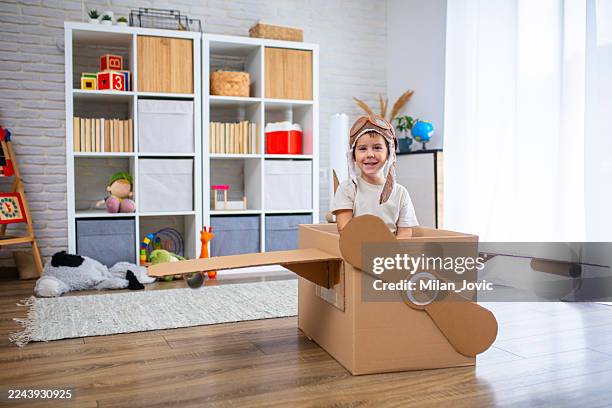 cute boy dressed as a pilot pretends to fly in a cardboard box airplane, showing creativity and childhood imagination. - aviation hat stock pictures, royalty-free photos & images