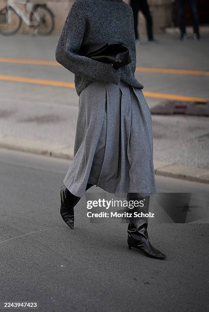 Mirja Klein is seen wearing a dark grey wool turtleneck sweater by Edited; a wool midi skirt in grey by Edited; black pointed leather knee-high boots...