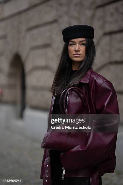 Amanda Azoitei is seen wearing a burgundy oversized faux leather jacket with silver details, a detachable belt and padded shoulders by The Frankie...