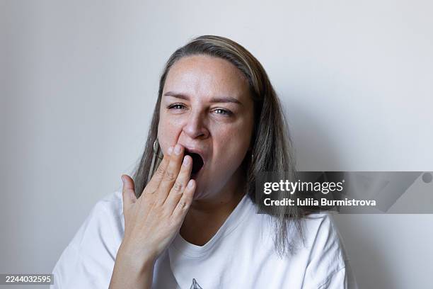yawning woman in white shirt expresses fatigue and morning tiredness in a casual portrait - tired eyes stock pictures, royalty-free photos & images
