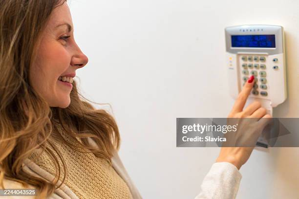 young smiling woman setting up home alarm and security system - burglar alarm stock pictures, royalty-free photos & images