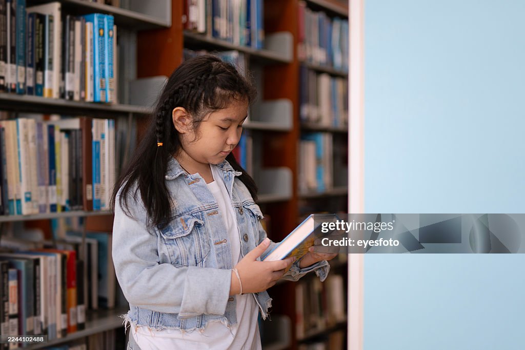 A young girl is reading the book at the library.