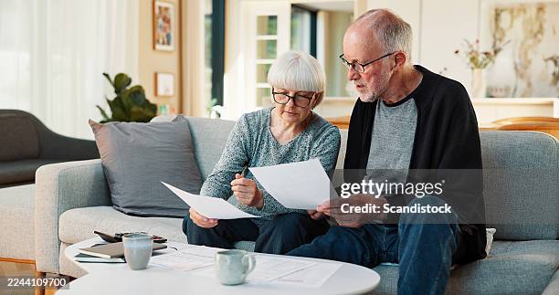 senior couple, sofa and finance with documents for budget planning, pension or retirement in home. elderly, man and woman with paperwork on couch for mortgage expenses, bills or payments in house - zorgverzekering stockfoto's en -beelden