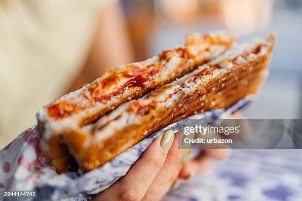 close-up of a young woman eating a sandwich while sitting outdoors at a fast food diner - toasted sandwich stock pictures, royalty-free photos & images