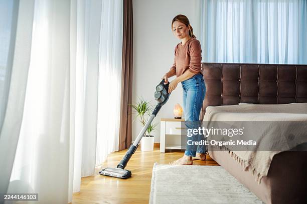 donna che pulisce il pavimento della camera da letto con l'aspirapolvere senza fili - aspirapolvere foto e immagini stock
