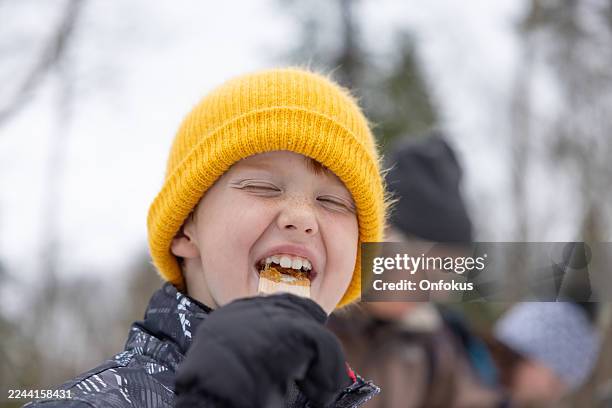 glücklicher junger junge probiert ahorn-zuckertoffee auf schnee in der zuckerhütte - bonbon stock-fotos und bilder