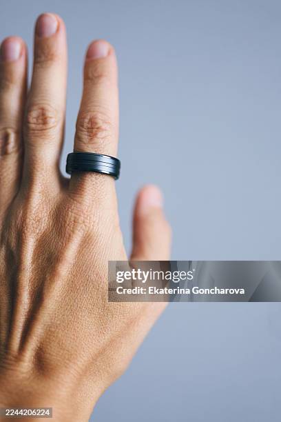 close-up of a hand with black ring on grey-blue background - bague photos et images de collection
