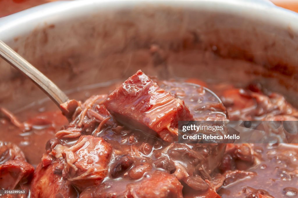 View from above, homemade Brazilian feijoada in a pot with a ladle showing some chopped beef and the beans that make up the stew.