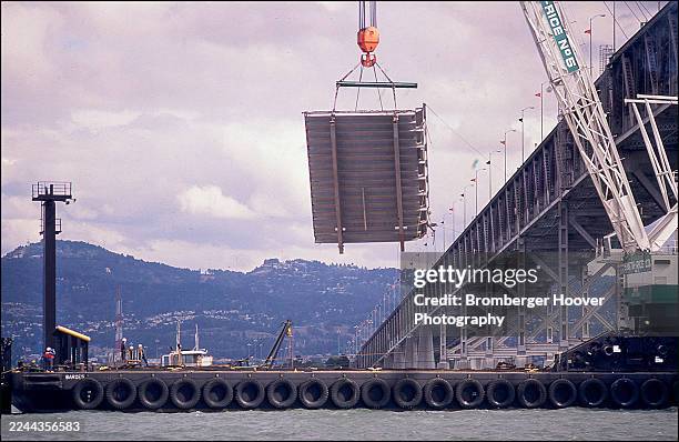 View of a 75-ton slab, from the upper deck of the San Francisco Bay Bridge, held aloft but a barge-mounted crane, in San Francisco Bay, San...